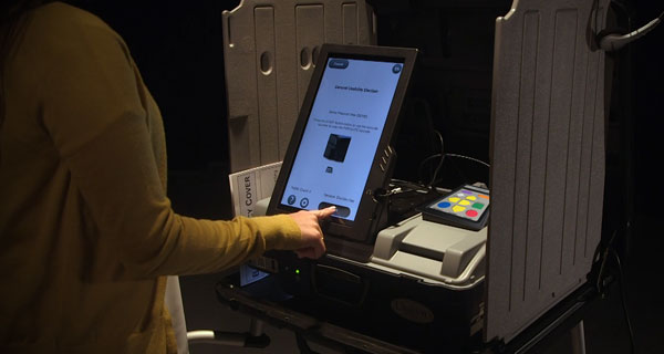 Voter touching the Start button on the Unisyn OpenElect ballot marking device with privacy screen.