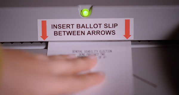 Paper ballot being inserted into the scanner between the arrows with a green light.